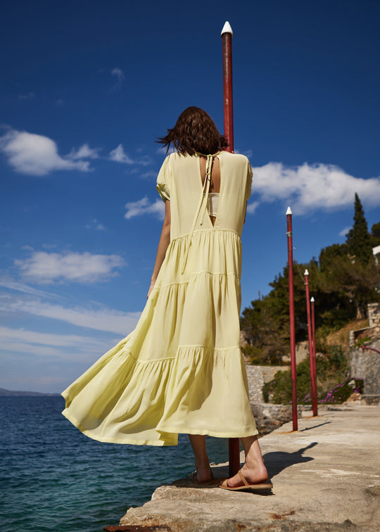 Girl in yellow dress standing by the sea on her back